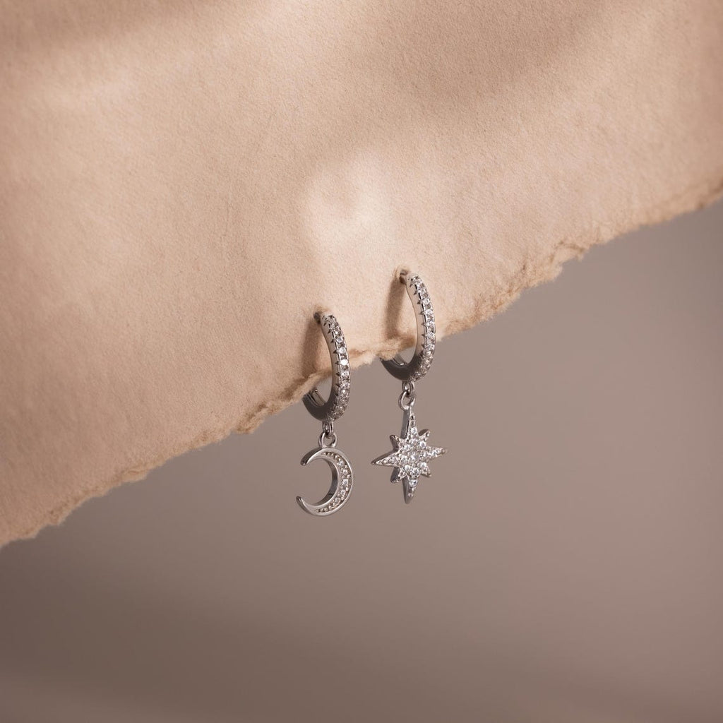 Silver hoop earrings with moon and star charms on a soft beige background