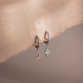 Silver hoop earrings with moon and star charms on a soft beige background