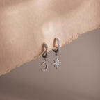 Silver hoop earrings with moon and star charms on a soft beige background