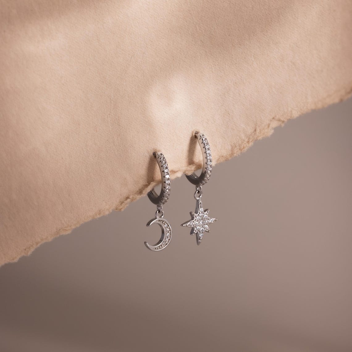 Silver hoop earrings with moon and star charms on a soft beige background