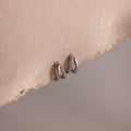 Pair of silver pave hoop earrings on a beige stone surface