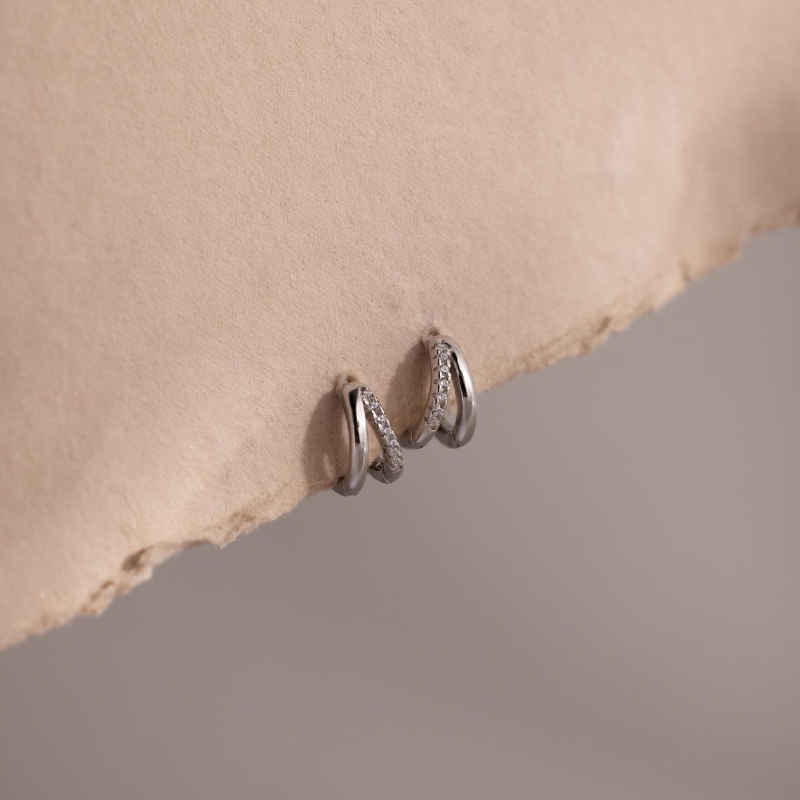 Pair of silver pave hoop earrings on a beige stone surface