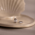 Two silver marquise diamond hoop earrings on a beige ceramic dish with a blurred background