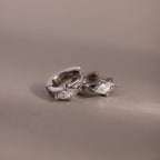 Pair of silver hoop earrings with marquise-shaped gemstones on a beige background
