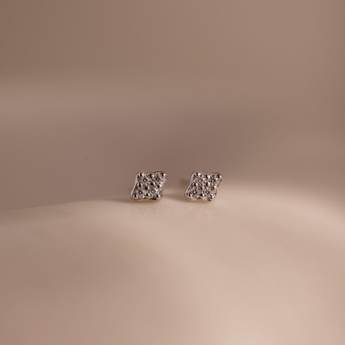 Pair of silver kite-shaped earrings with embedded stones on a beige background
