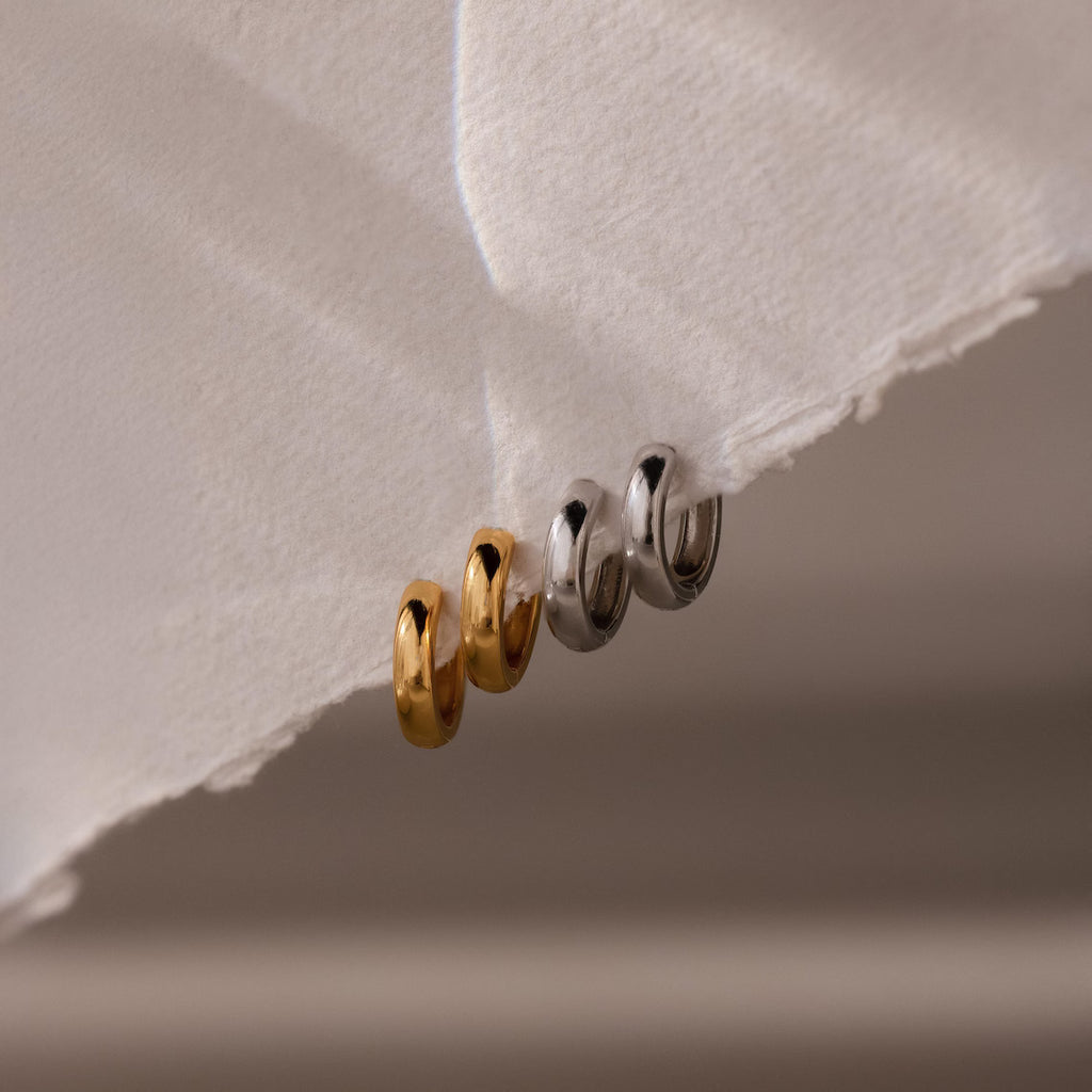 Two gold and two silver hoop earrings on a textured white surface