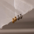 Two gold and two silver hoop earrings on a textured white surface
