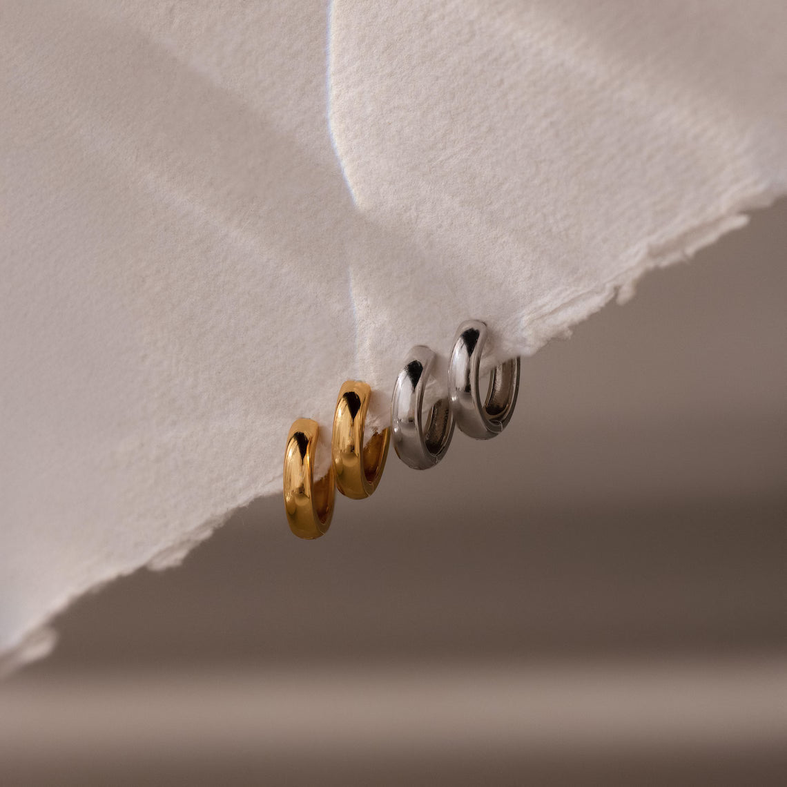 Two gold and two silver hoop earrings on a textured white surface