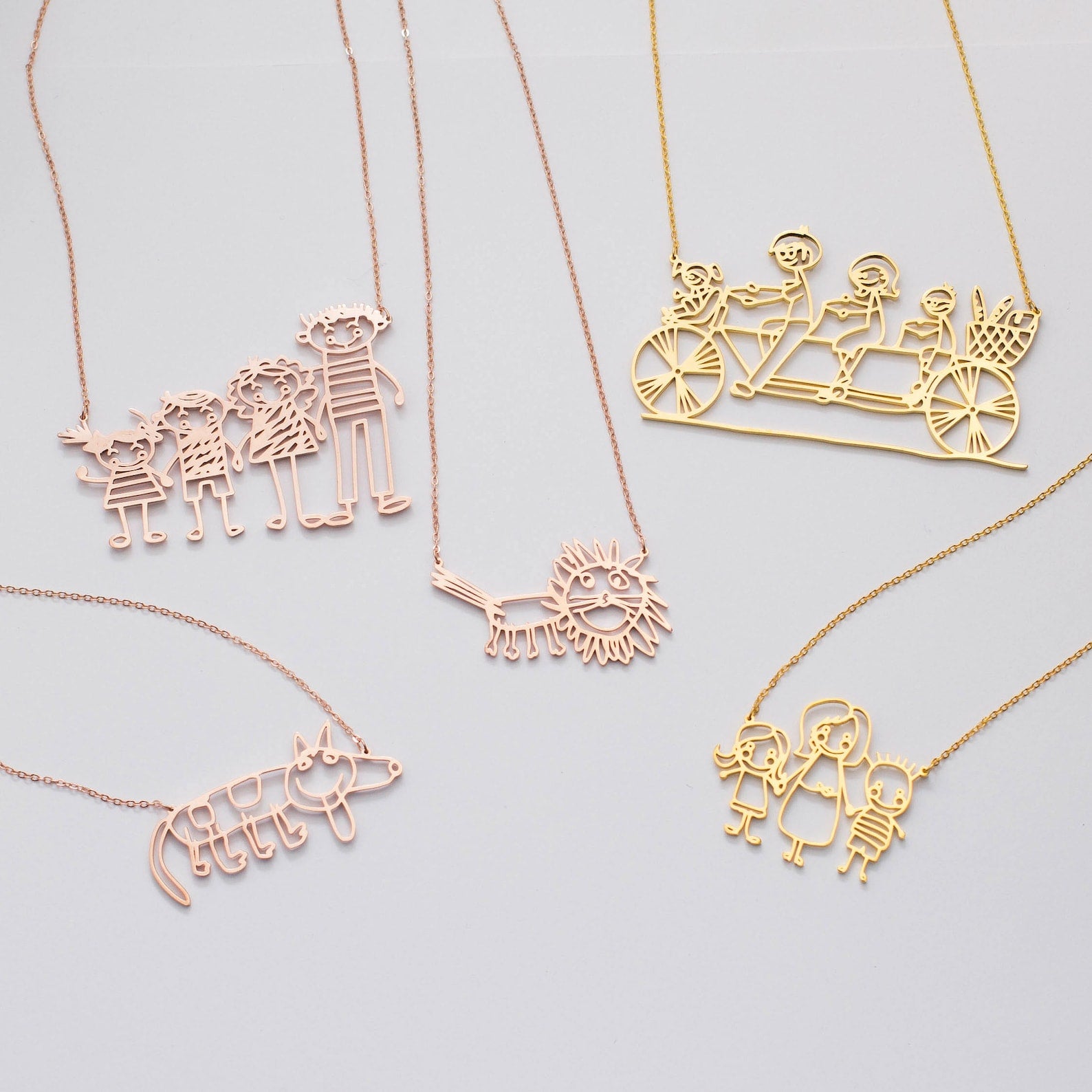Five Kids Drawing Necklaces—shaped like families, a lion, a cat, and people on a tandem bicycle—are displayed as unique Wearable Art, perfect for personalized gifts or custom jewelry inspired by children's drawings.