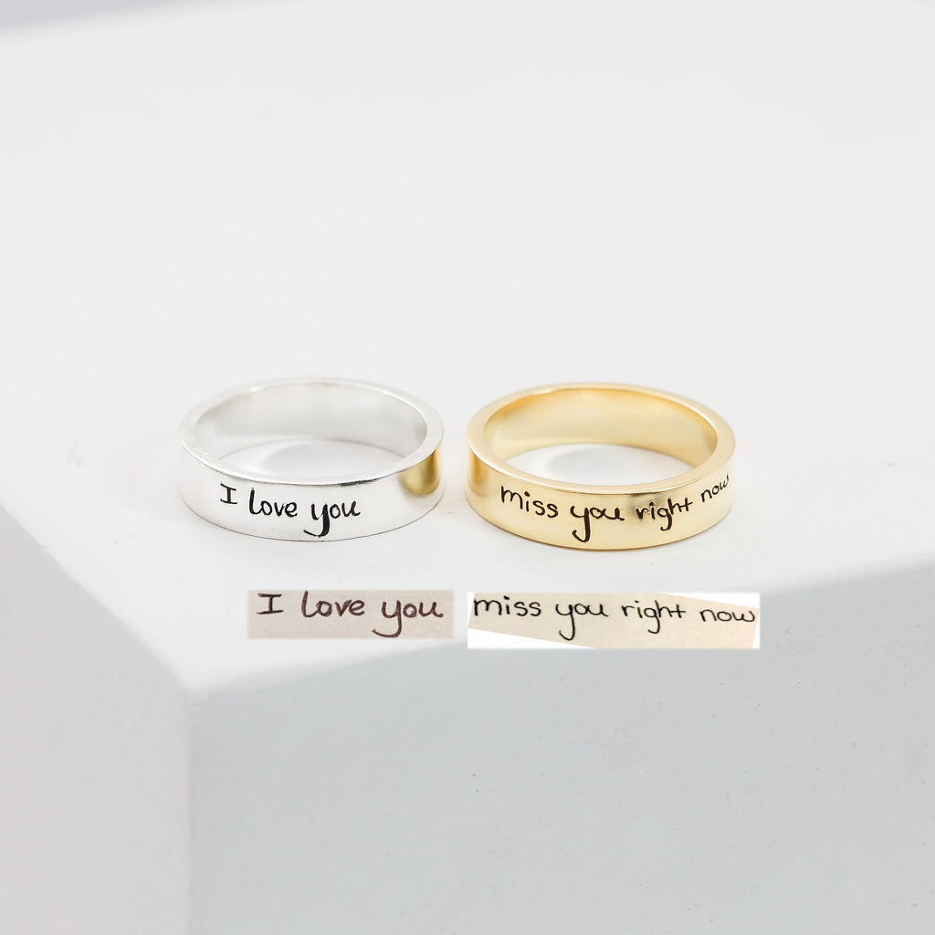 A silver Handwriting Band engraved with "I love you" and a gold custom ring with "miss you right now" rest on a white surface—ideal as heartfelt Christmas gifts.