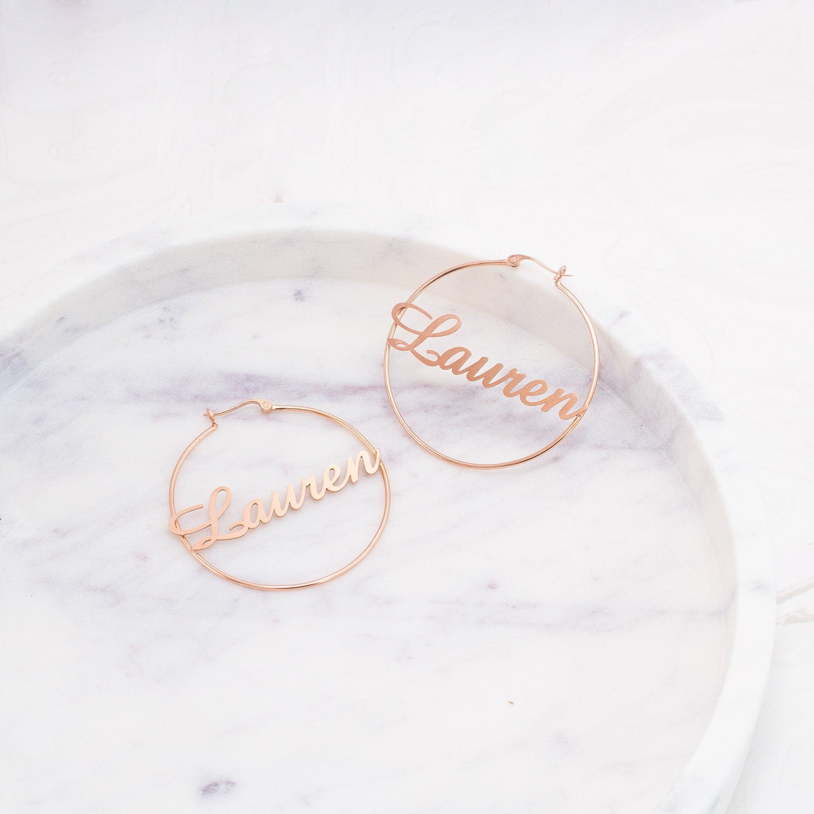 Personalized jewelry at its finest—these Classic Name Hoops feature "Lauren" in elegant script, beautifully showcased on a round marble tray.