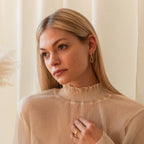 Woman with long blonde hair wears a sheer beige top and the Linked Necklace & Earrings Set, paired with a ring, looking thoughtful.