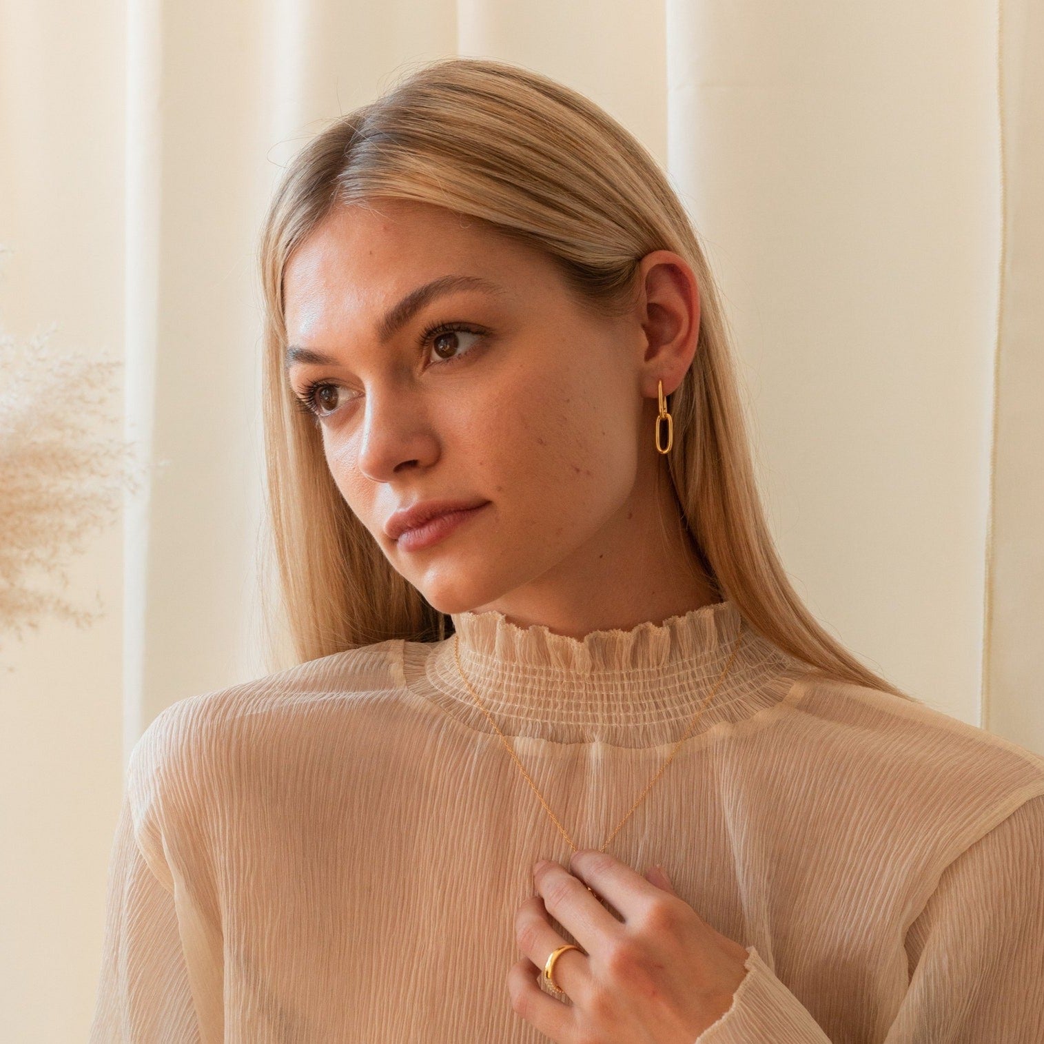 Woman with long blonde hair wears a sheer beige top and the Linked Necklace & Earrings Set, paired with a ring, looking thoughtful.