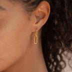 Close-up of a person wearing a gold oval-shaped hoop earring from the Linked Necklace & Earrings Set, with curly hair in the background.