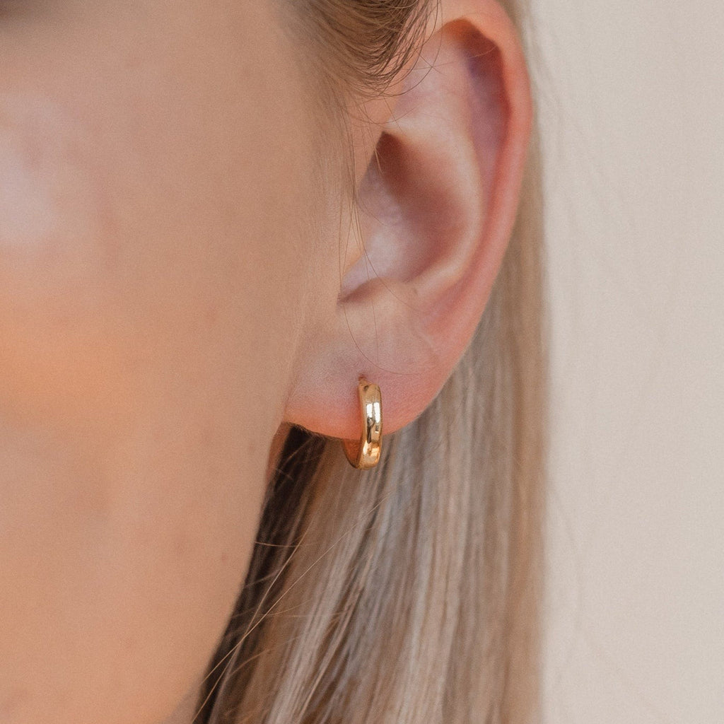 Close-up of a woman's ear wearing Editor II Huggies in sterling silver, classic hoop earrings, with blonde hair partially visible.