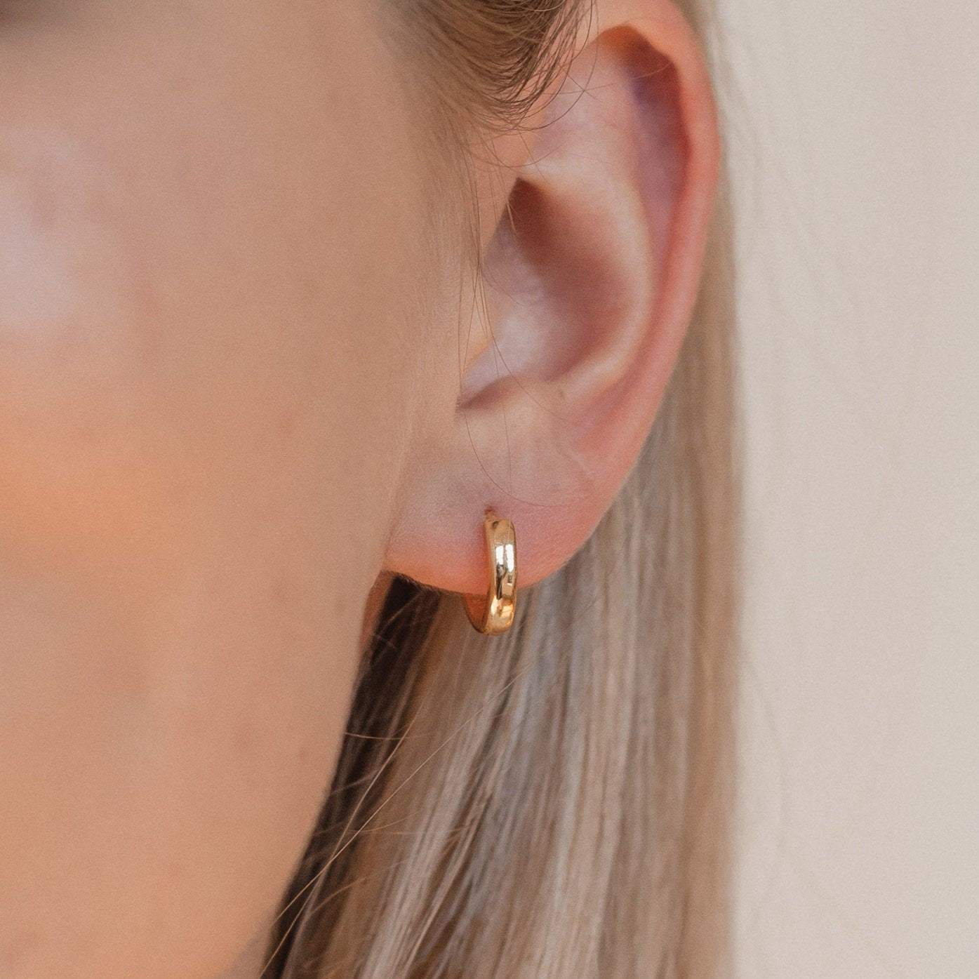 Close-up of a woman's ear with straight blonde hair, wearing Editor II Huggies—timeless hoops designed for everyday style.