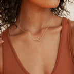 Woman wearing a rust-colored tank top and the Linked Charm Necklace and Earrings Set in 18K Gold, cropped at the shoulders.