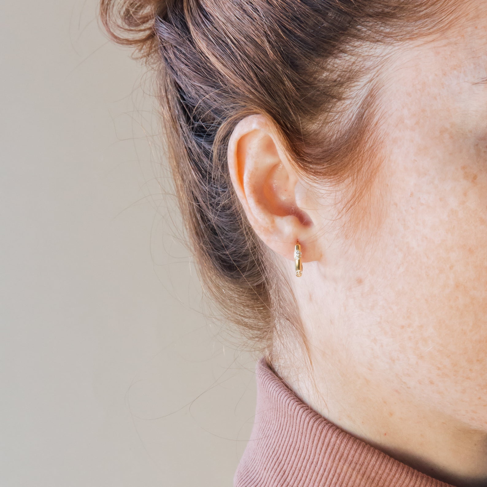 Close-up of a model wearing a gold diamond hoop earring with a neutral background