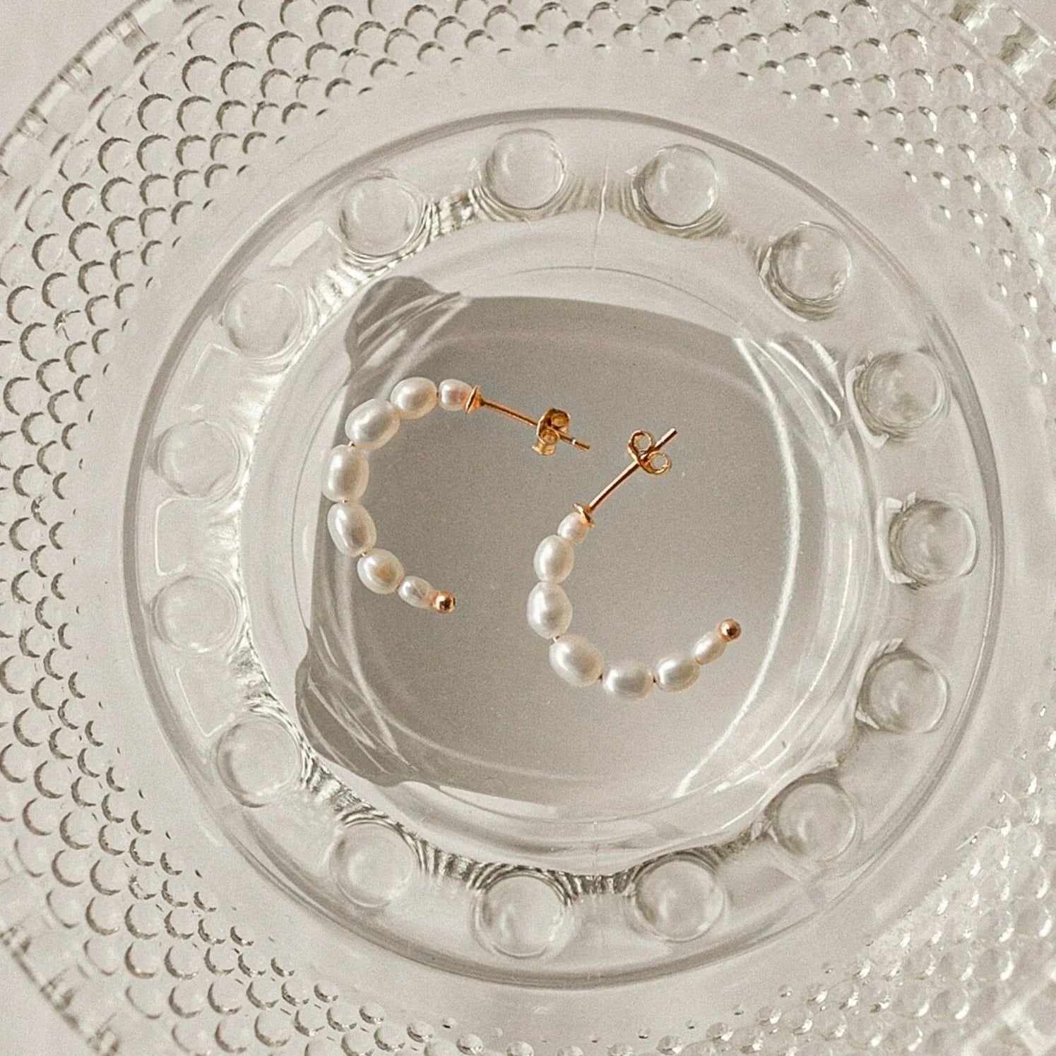 The Pearl Earrings Set is elegantly displayed on a clear, textured glass plate.