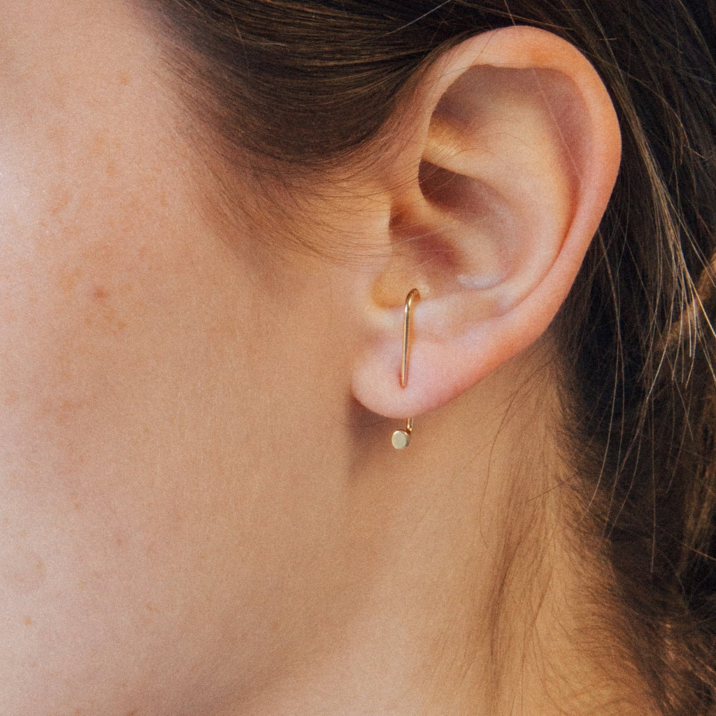 Close-up of a model wearing a minimalist gold ear jacket style earring.