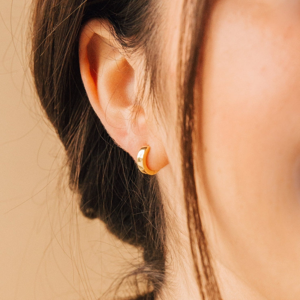 Close-up of a woman's ear adorned with Meg Huggies in 18K Gold, her brown hair tucked behind her ear for a simple yet elegant look.