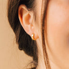 Close-up of a woman's ear adorned with Meg Huggies in 18K Gold, her brown hair tucked behind her ear for a simple yet elegant look.