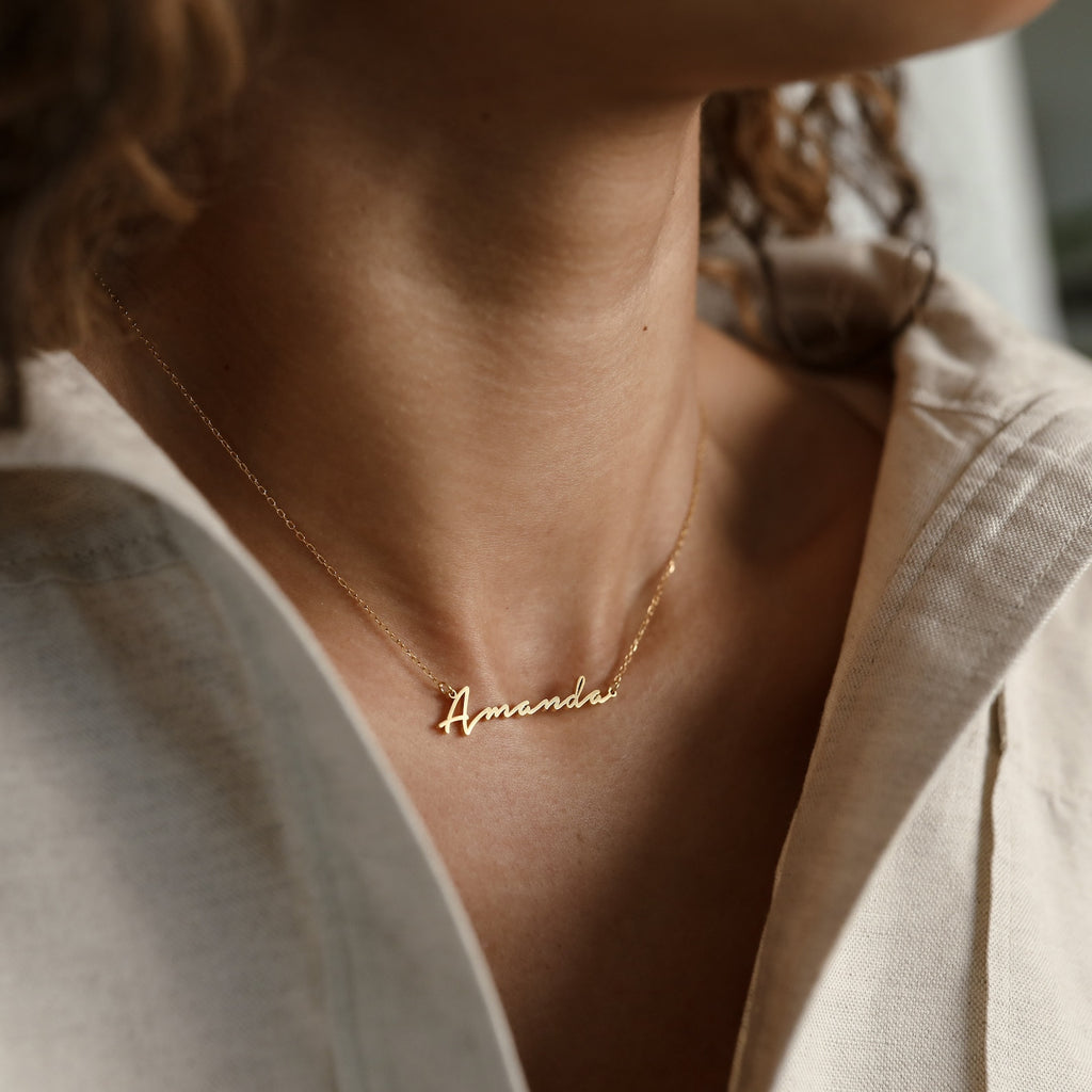 A woman wearing the Summer Name Necklace personalized with "Amanda" in a script font, paired with a light-colored top.