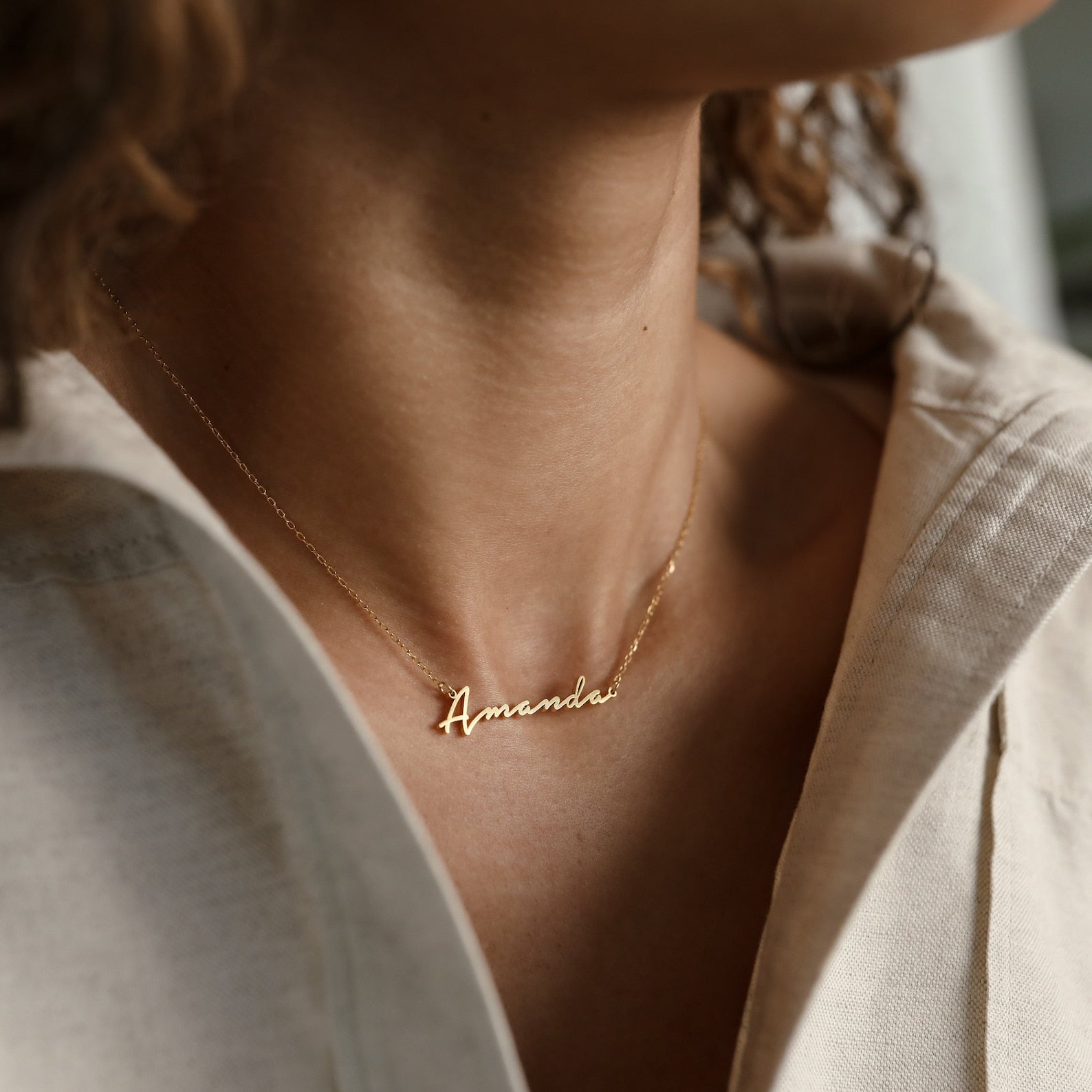 A woman wearing the Summer Name Necklace personalized with "Amanda" in a script font, paired with a light-colored top.