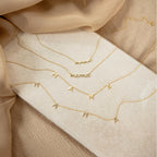 Four Mama Letter Necklaces rest on a beige surface among soft tan and beige fabric—an ideal mother gift and a lovely way to celebrate motherhood.