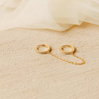 Gold pave hoop earrings with a chain on a beige fabric background