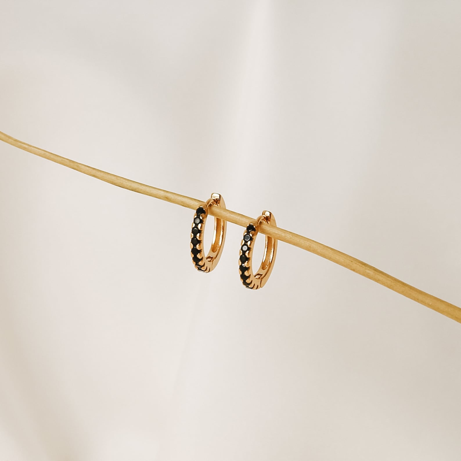 Black Onyx Hoops Bundle: gold hoop earrings with small black onyx stones, displayed on a thin beige stick against a light background.