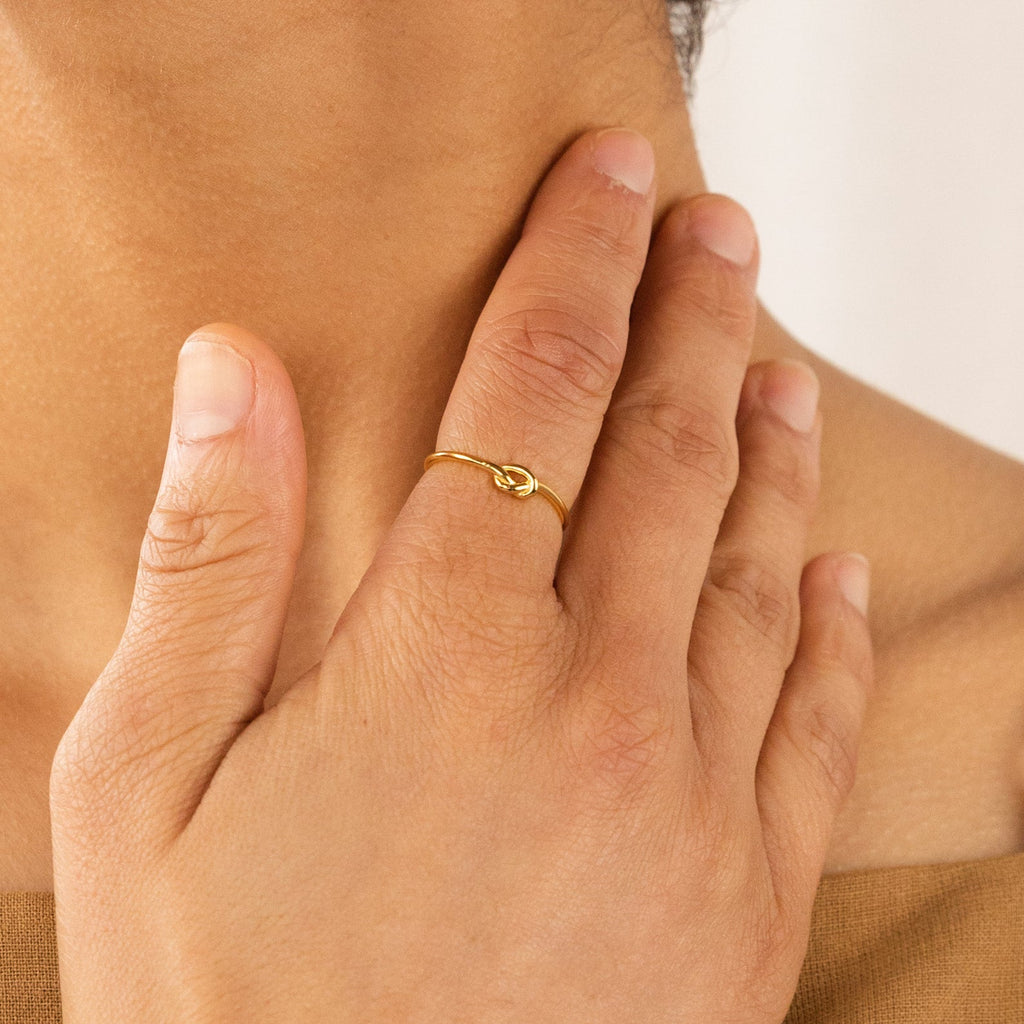 A hand wearing the Knot Ring in Sterling Silver rests on a person’s neck, forming a symbolic gesture against a neutral background.