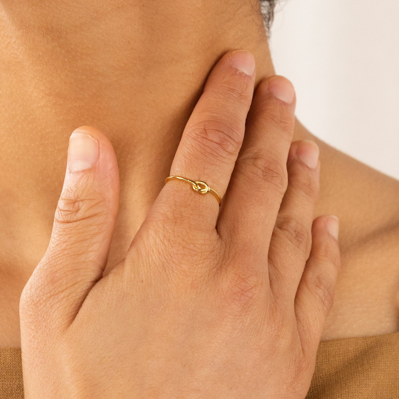A hand wearing the Knot Ring in Sterling Silver rests on a person’s neck, forming a symbolic gesture against a neutral background.
