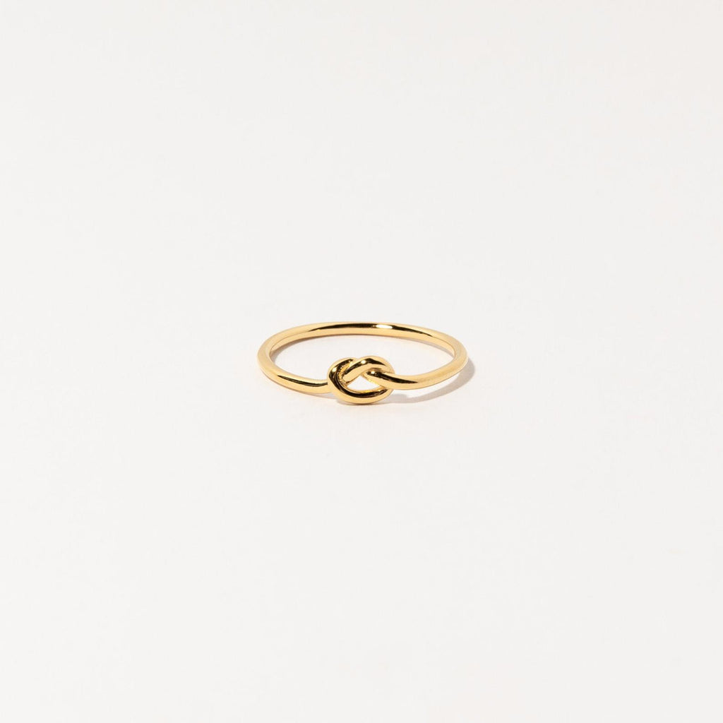 The Knot Ring in 18K Gold features a delicate knot design at the center, shown on a white background—ideal as a meaningful symbol or an elegant wedding gift.