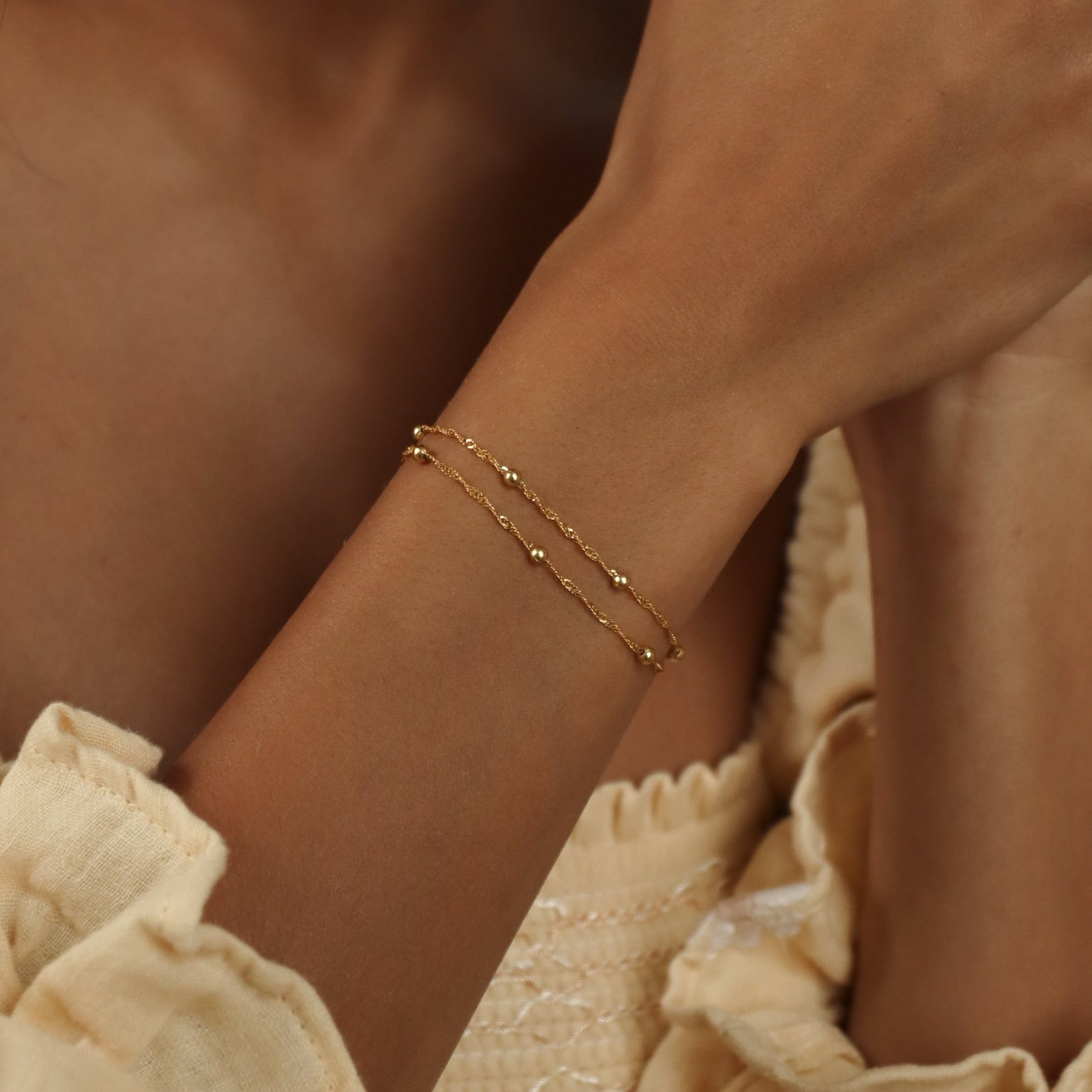 A person wearing the Duo Bead Chain Bracelet and a light cream, textured top.