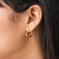 Close-up of a model wearing a gold heart hoop earring with dark hair partially visible.