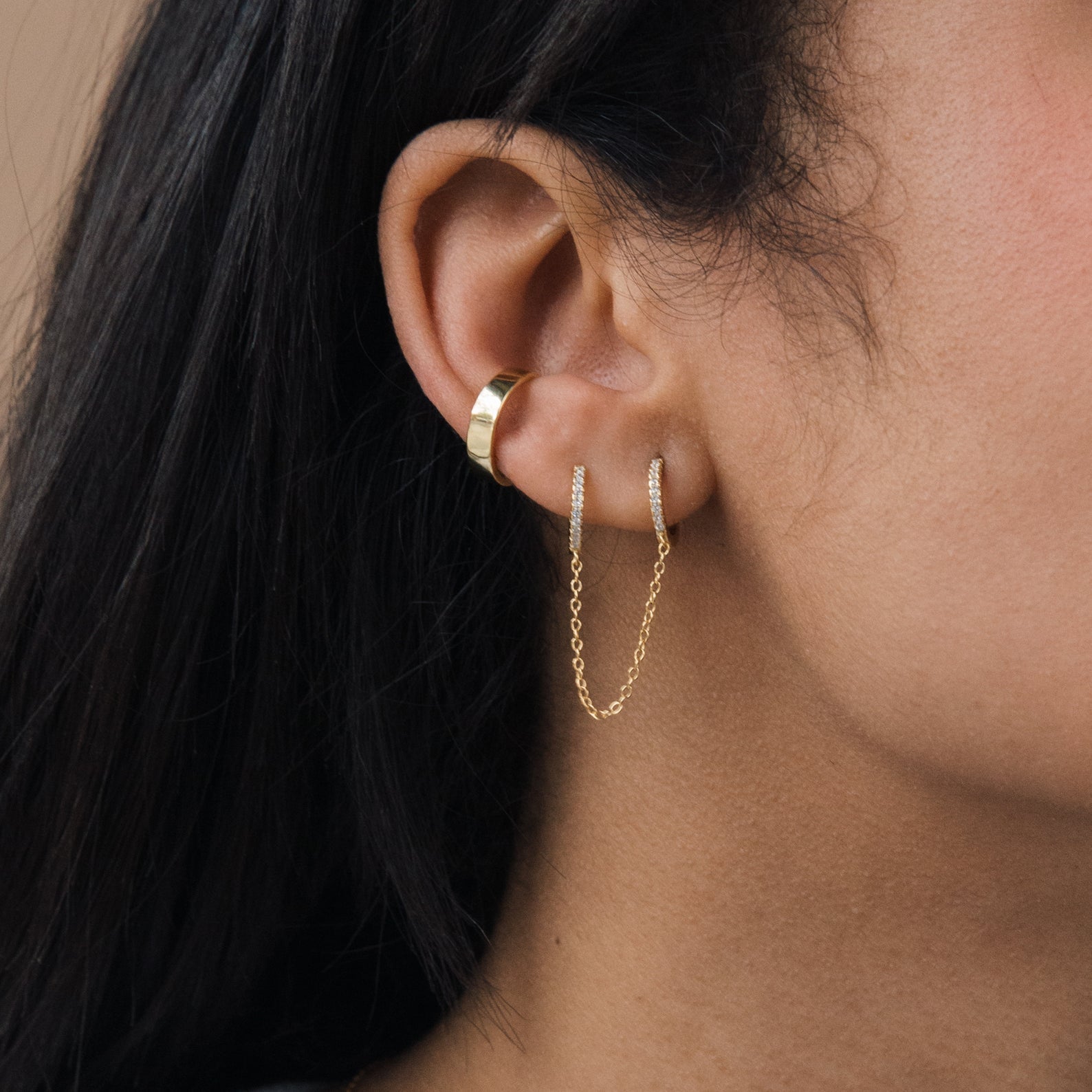 Close-up of a model wearing gold hoop earrings with a neutral background