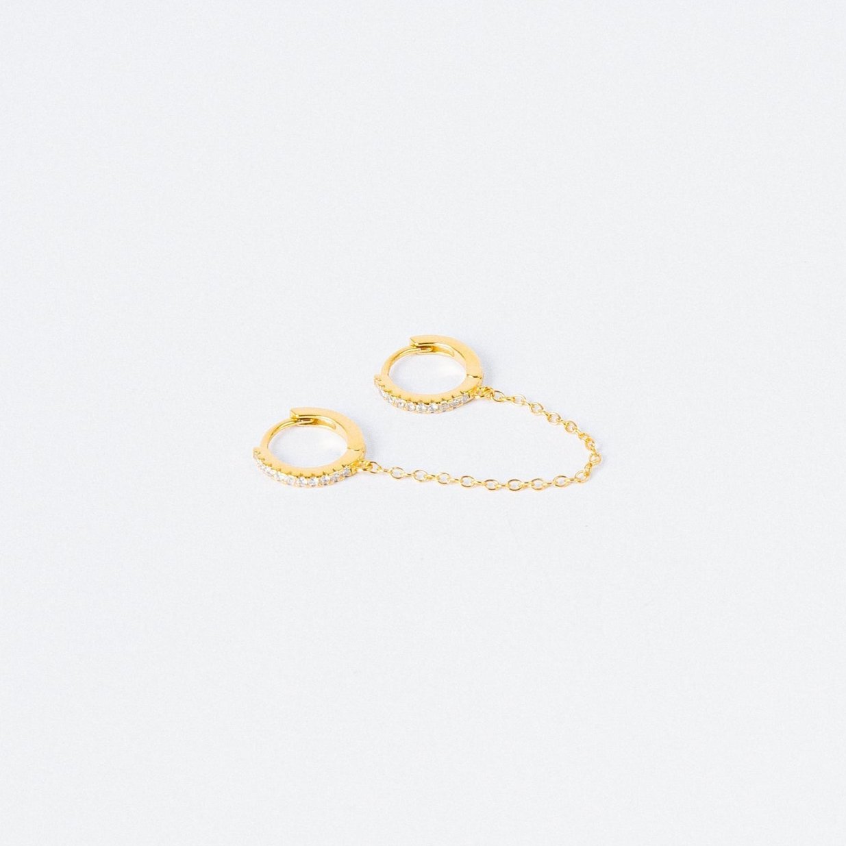 The Diamond Chain Earrings Set features two small gold hoops linked by a delicate chain, each adorned with clear stones for extra sparkle.