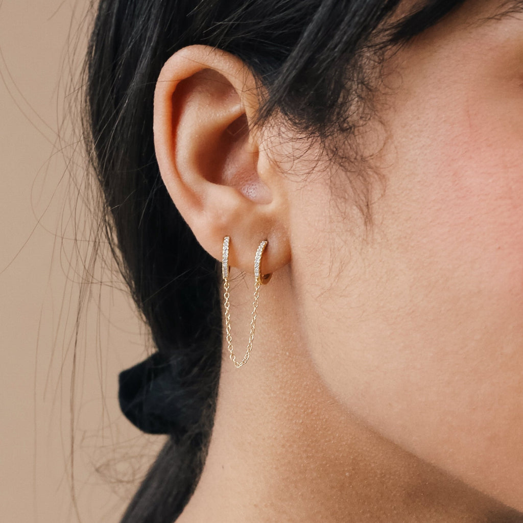 Close-up of a model wearing gold diamond hoop earrings with a neutral background