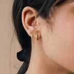 Close-up of a model wearing gold diamond hoop earrings with a neutral background