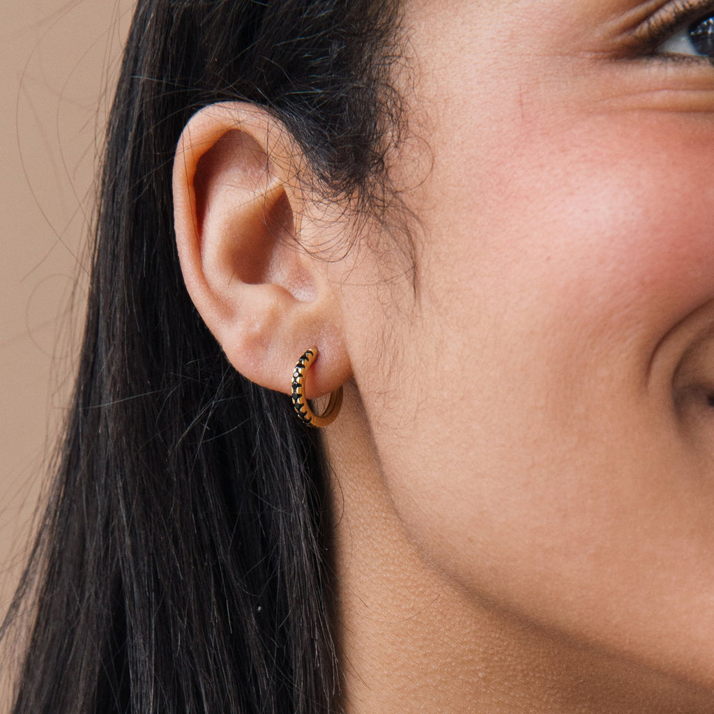 Close-up of a woman smiling, wearing Black Onyx Hoops Bundle—small gold hoops with black stones.