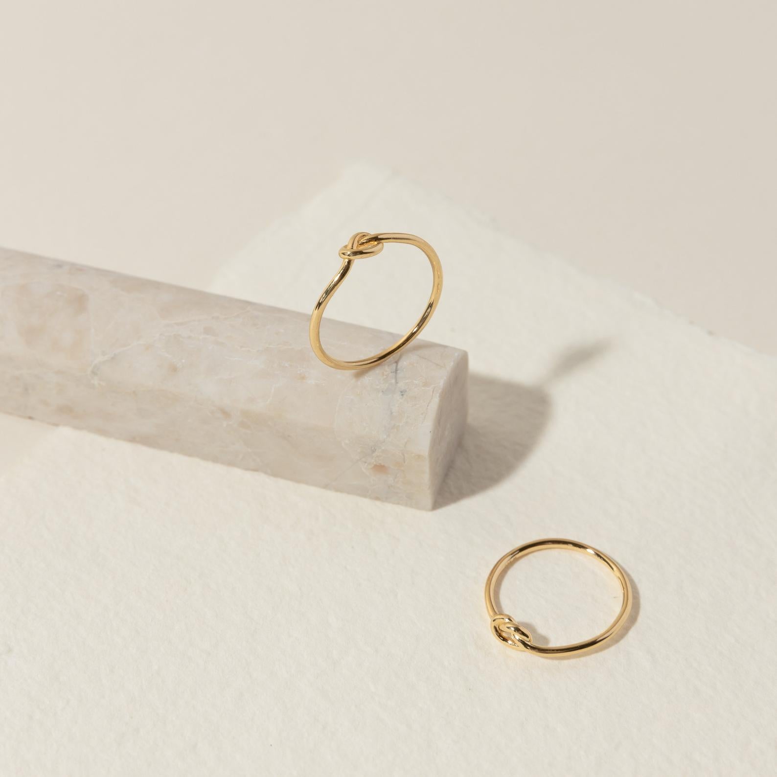 Two Knot Rings, symbolizing connection, are shown on a textured white surface and marble block—an ideal meaningful gift.