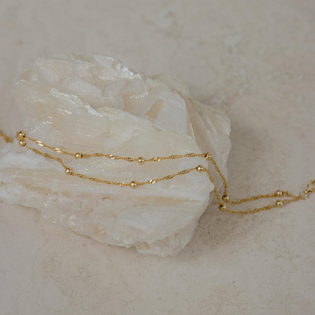Delicate gold chain necklace with small beads draped over a light crystal—pair it with the Duo Bead Chain Anklet for a cohesive, boho-inspired style.