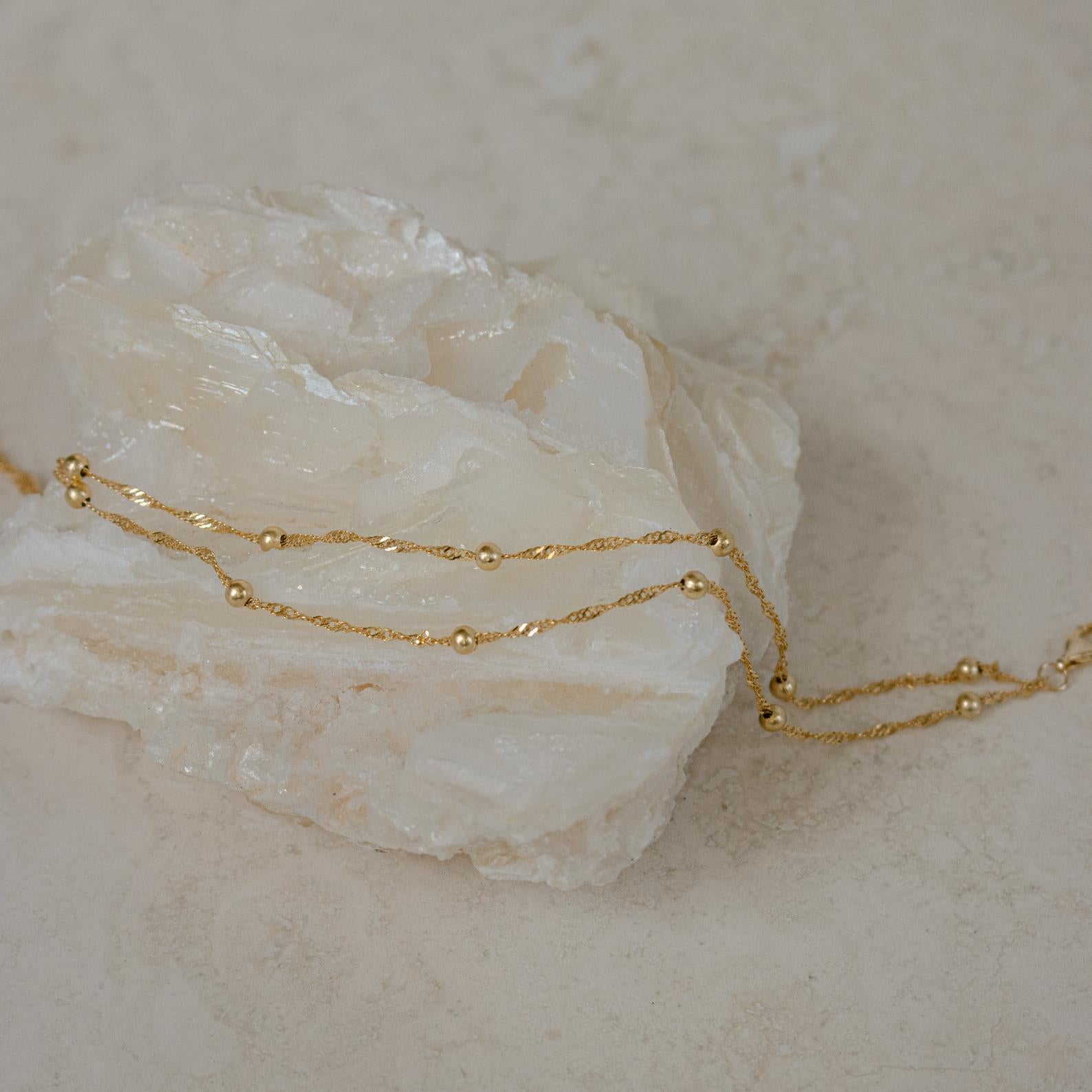 Delicate gold chain necklace with small beads draped over a light crystal—pair it with the Duo Bead Chain Anklet for a cohesive, boho-inspired style.