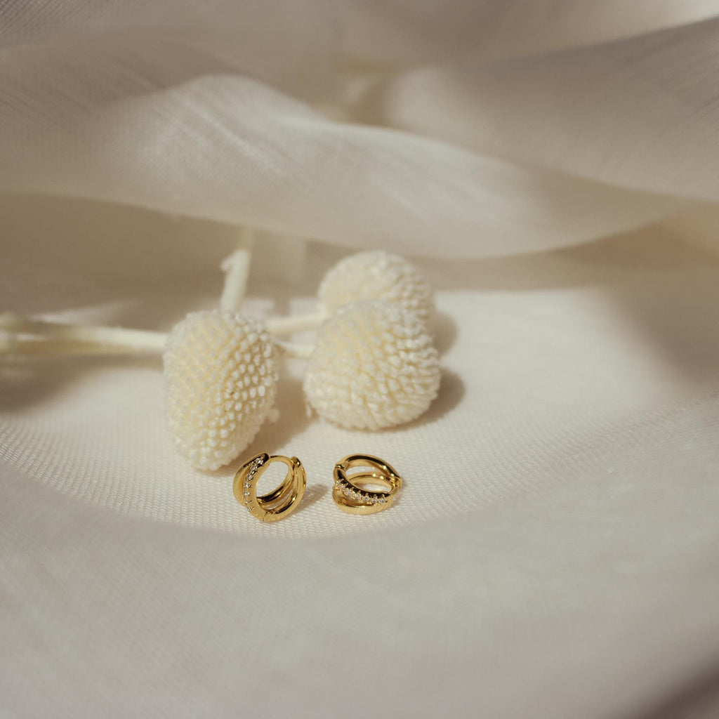 Flat lay of Amelia Duo Huggies on cream fabric with textured floral props.