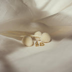 Pair of Amelia Duo Huggies resting near cream floral decor on satin fabric.