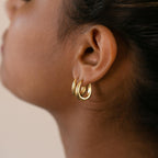 Close-up of a person's ear adorned with two Paris Oval Hoops in 18K Gold, showcasing elegant and classic gold earrings.