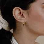 Close-up of a woman's ear wearing Paris Oval Hoops, with dark hair tied back in a light scarf.