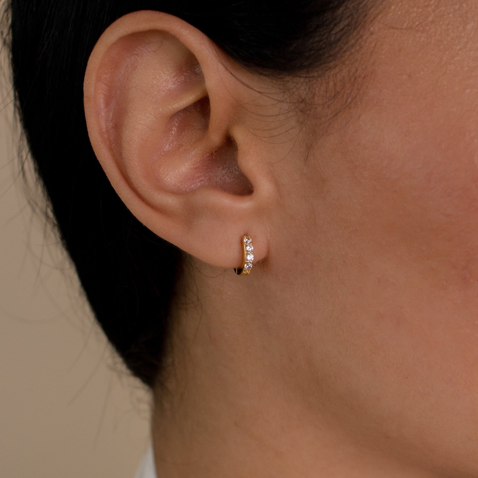 Close-up of an ear wearing Elise Diamond Huggies—small gold hoops with embedded white gemstones that showcase the subtle elegance of pave earrings.