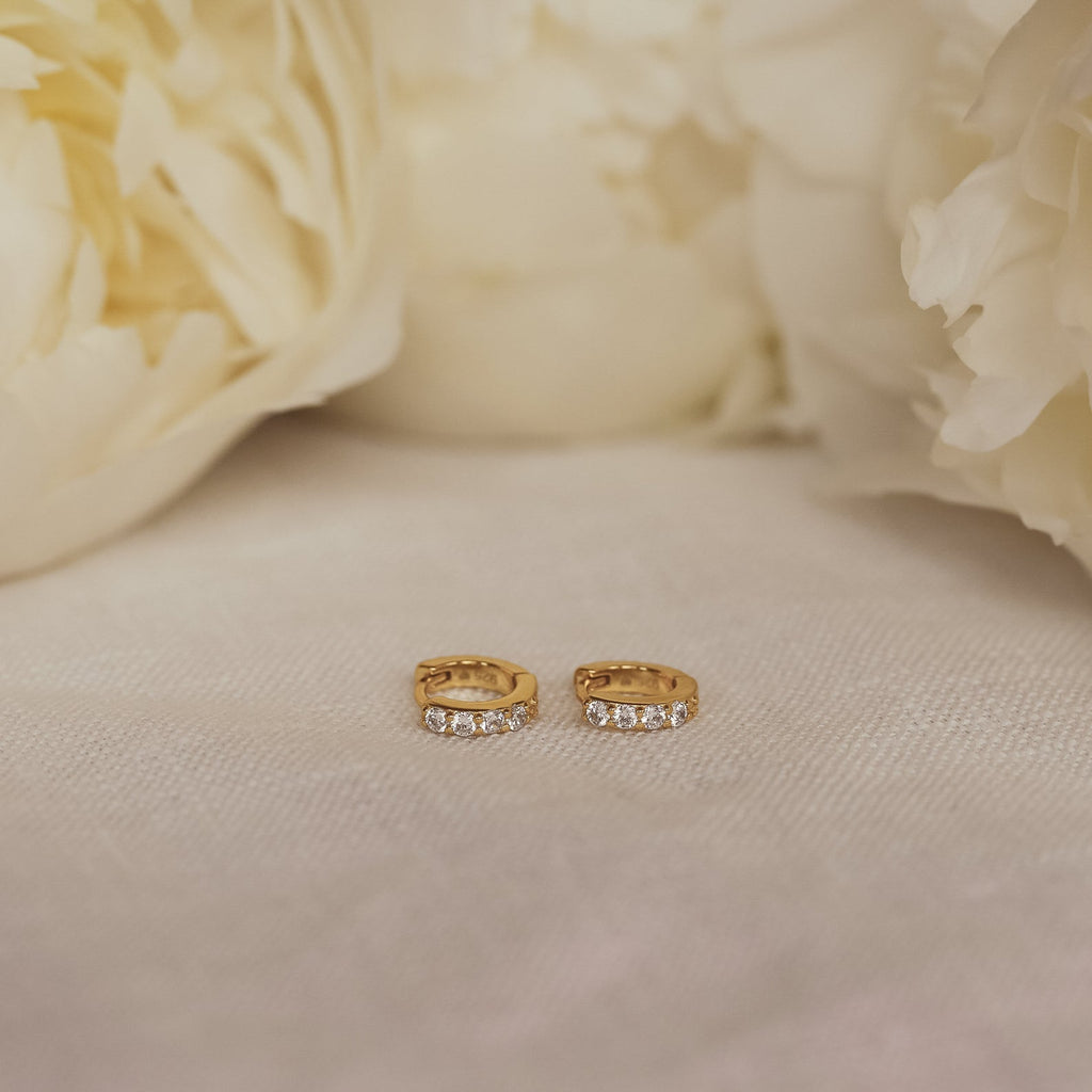 Elise Diamond Huggies in Sterling Silver, displayed on light fabric with white flowers—perfect subtle earrings for any occasion.